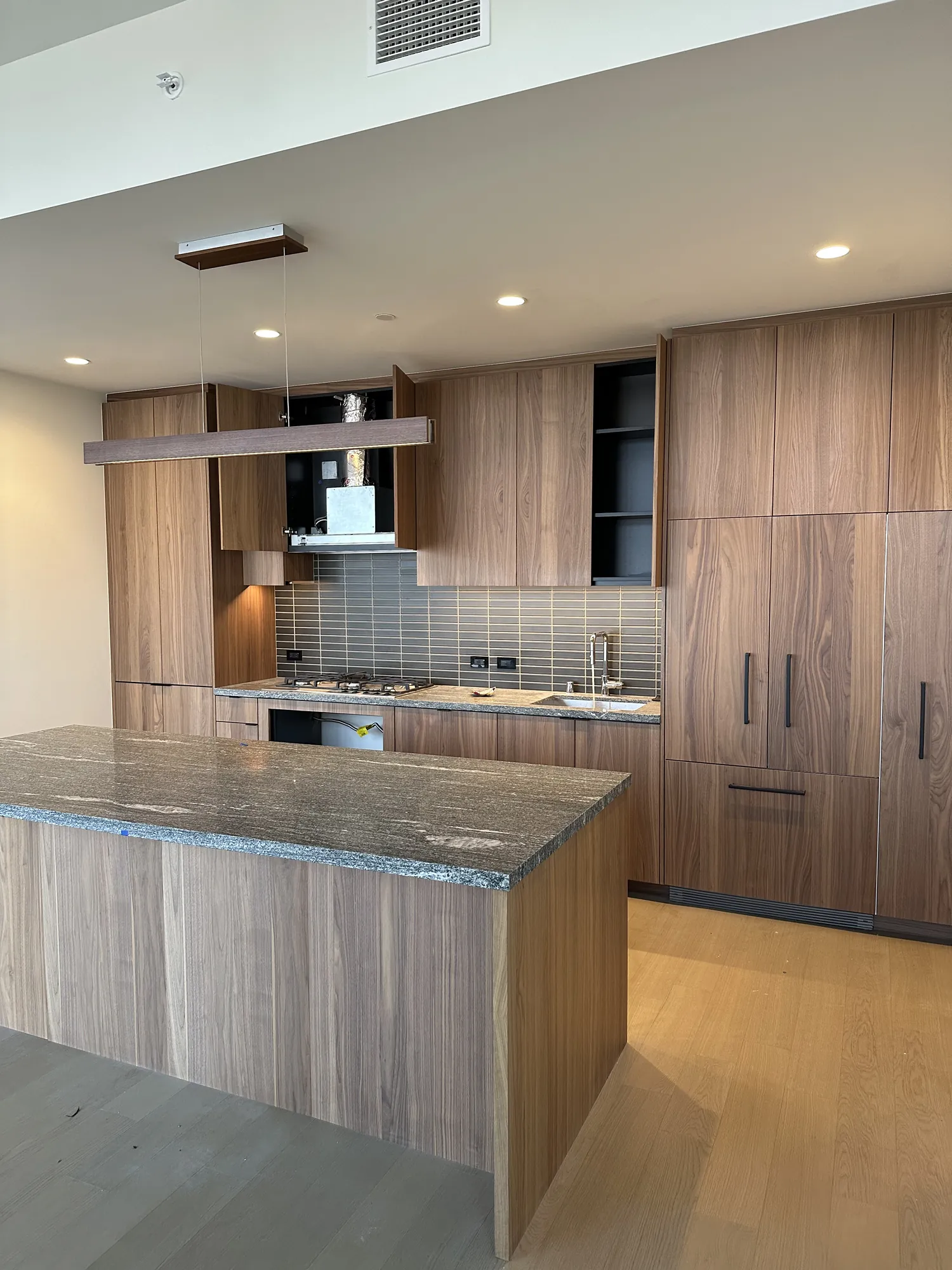 Luxury custom kitchen with walnut cabinetry, stone island and integrated sink plumbing by Poseidon Plumbing in Southern California